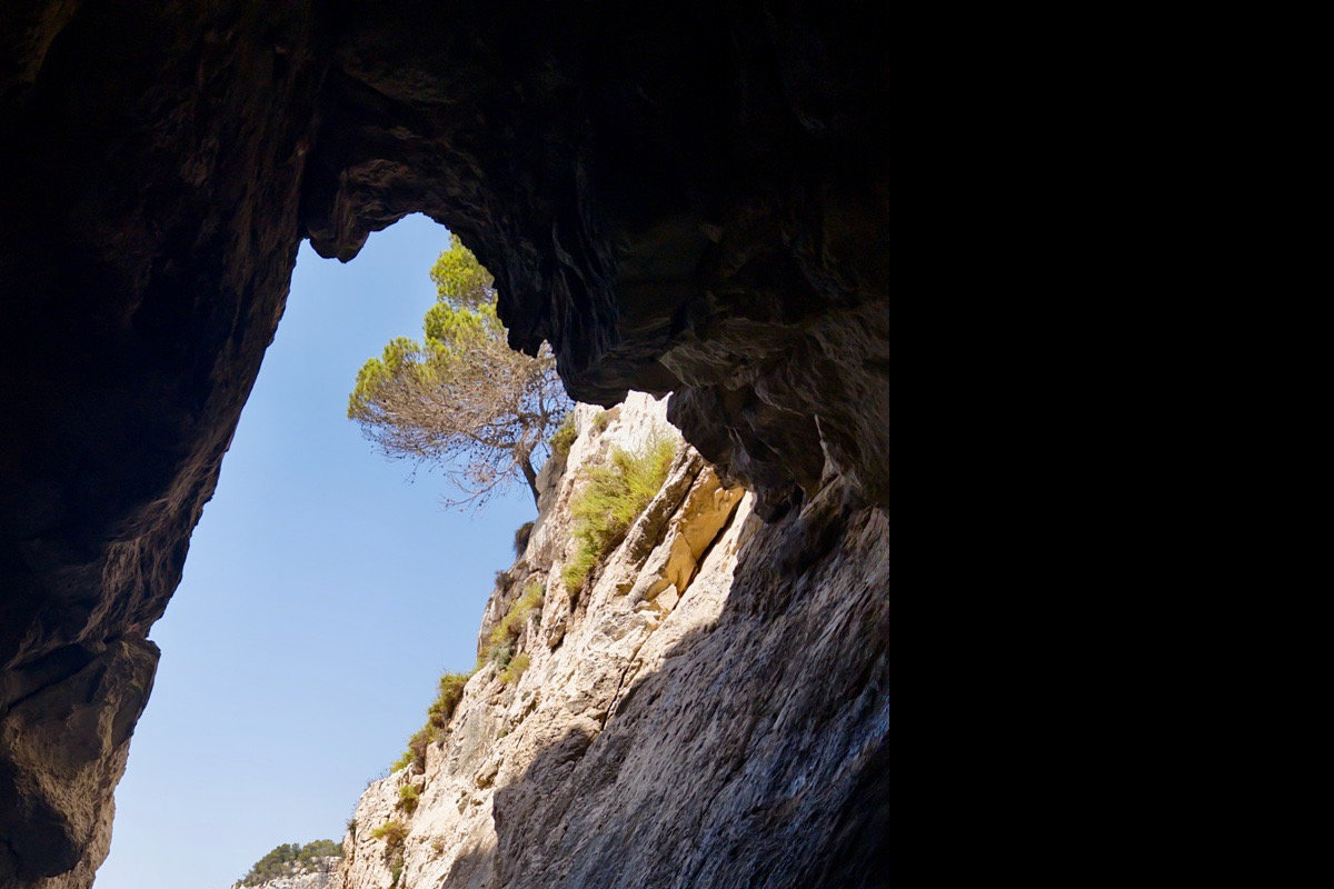 Sea cave arch at Cala Galdana looking out to turquoise water with anchored boats