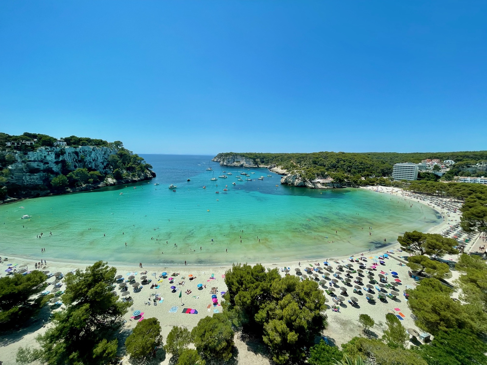 Aerial view of Cala Galdana bay full of sunbathers and boats in summer