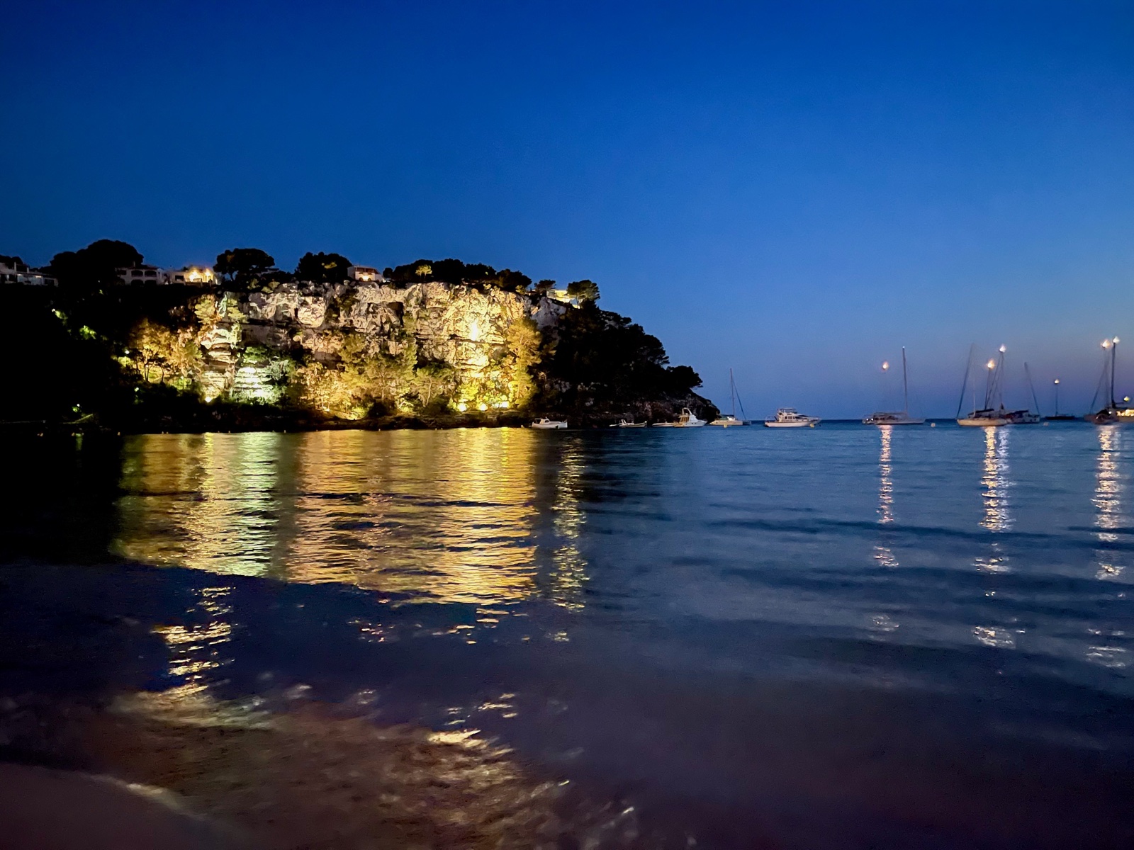 Cala Galdana bay at night — illuminated limestone cliffs reflecting in calm water