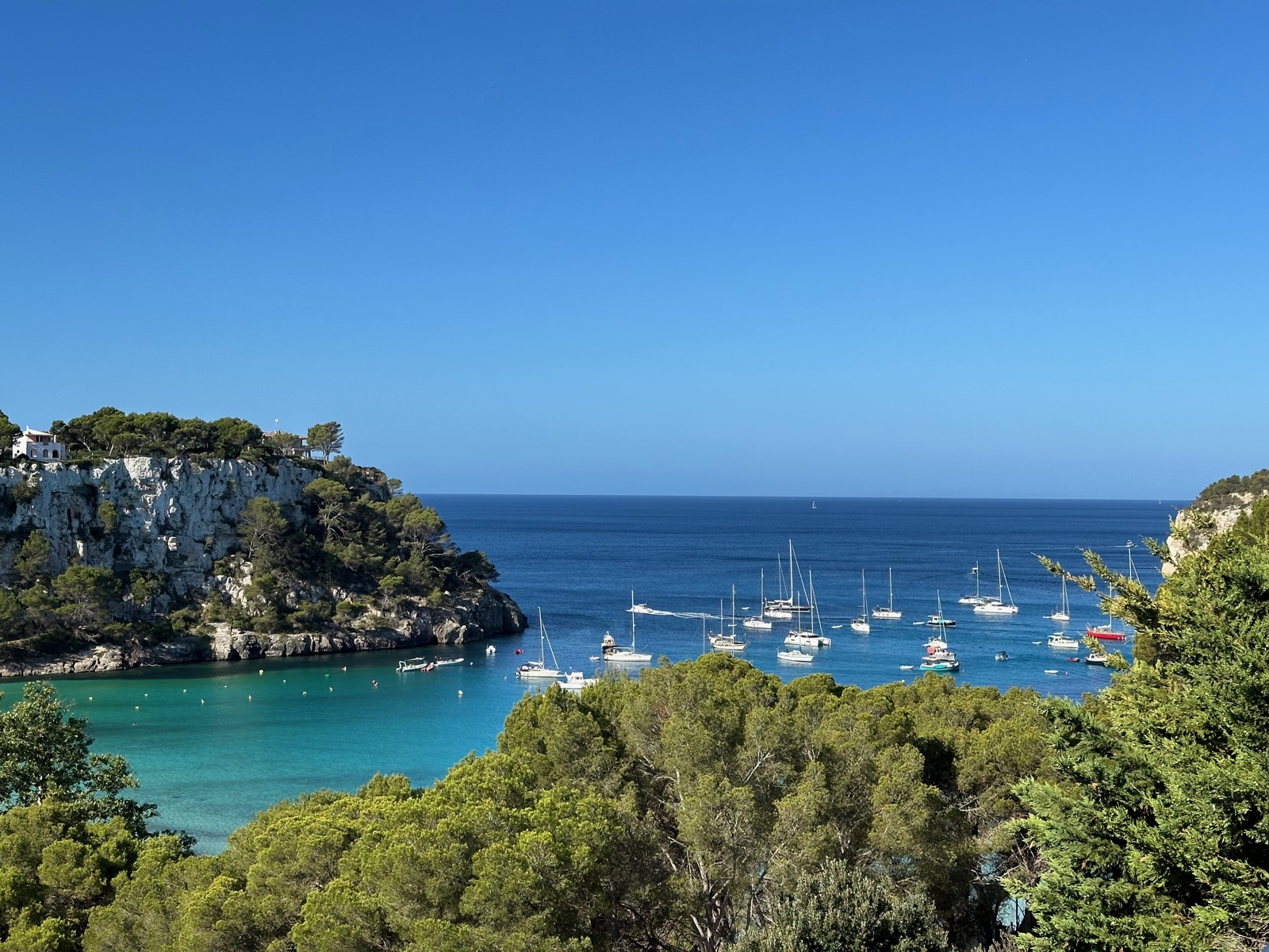 Cala Galdana bay with sailboats anchored in turquoise waters, viewed from above