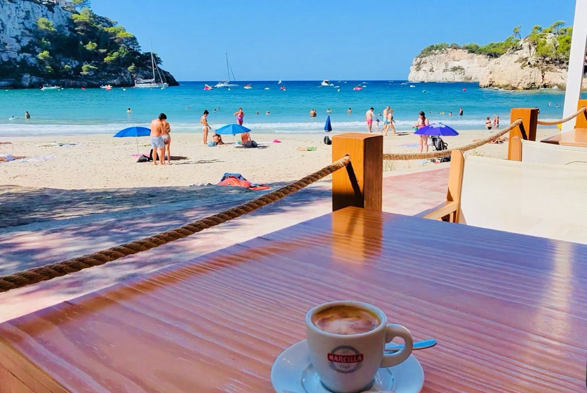 Coffee on a beachside terrace table overlooking Cala Galdana beach